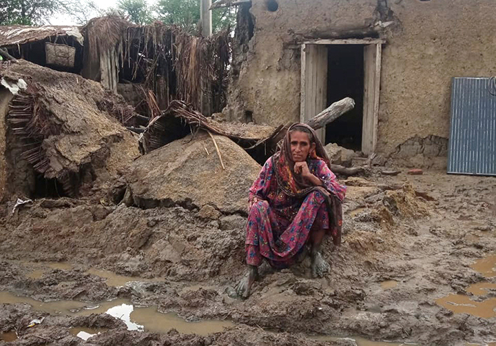 A woman sits in front of a collapsed house.