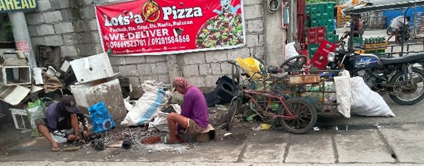 ジャンクショップ店先でモーターを解体し、排水溝に廃油を流している作業風景