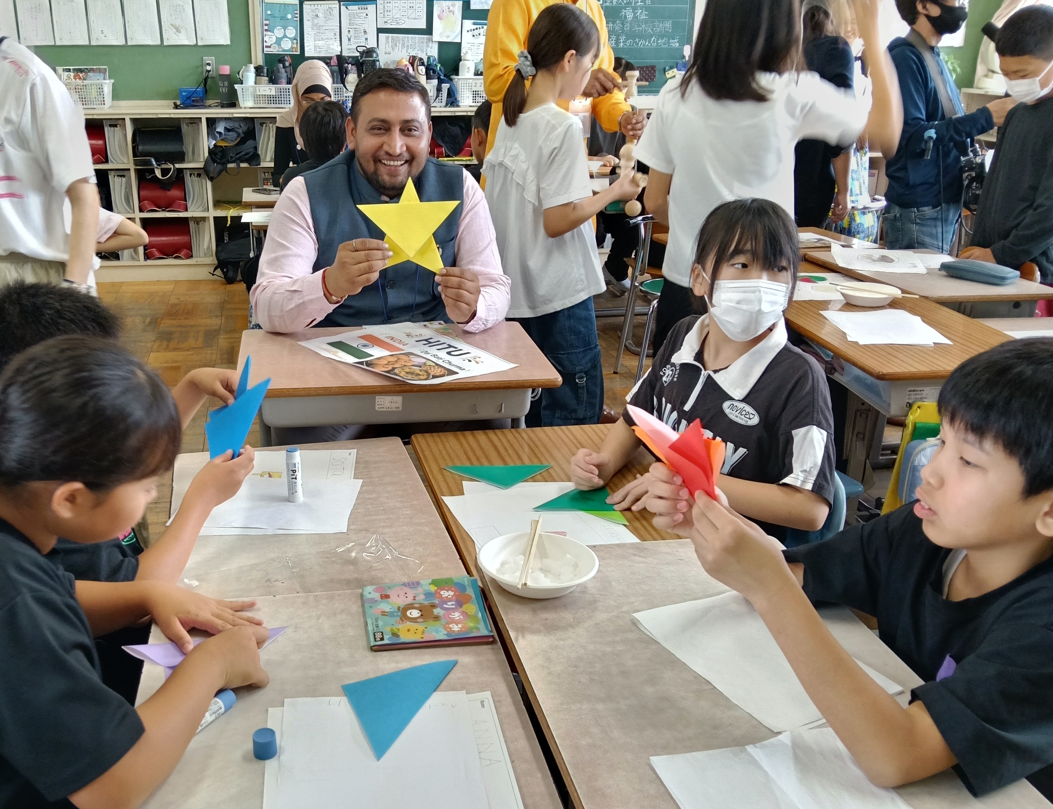 （写真⑦）：折り紙を教える児童たち①