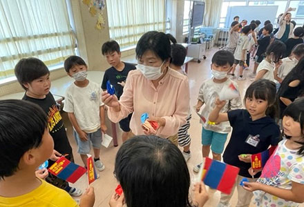 Ms. Purevjav (center) and Japanese children, actively communicating in their newly-learned Mongolian language and waving a handmade Mongolian flag (at Elementary School in Niigata City)