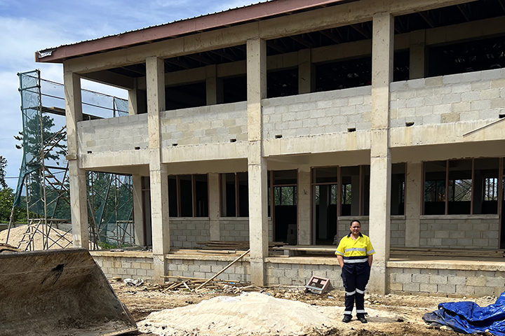 Victorina stands in front of a two-story reinforced concrete building currently under construction.