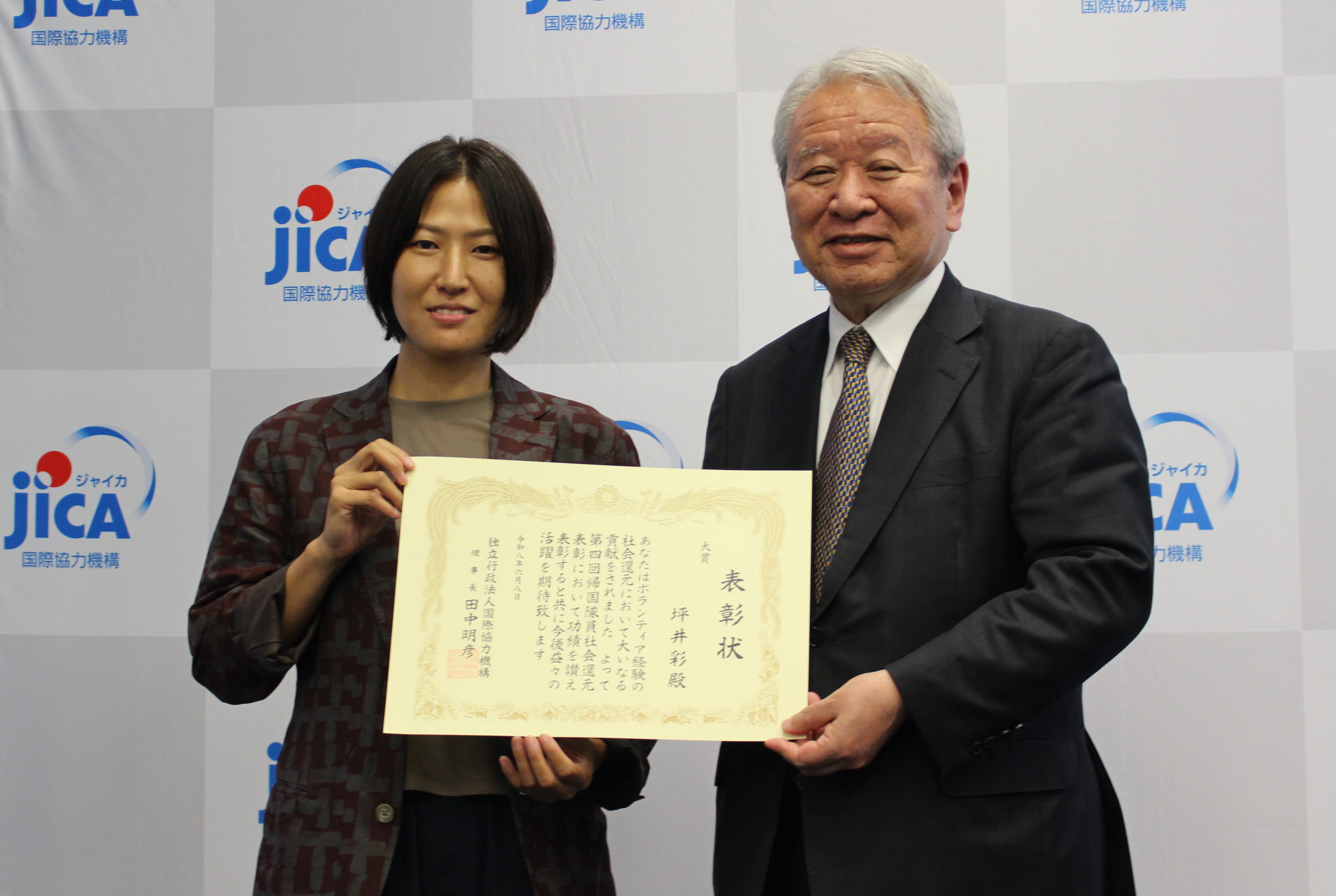 Tsuboi, left, stands alongside JICA President Tanaka Akihiko holding a certificate naming her the recipient of the grand prize in the 4th JOCV Commendation for Giving Back to Society awards.