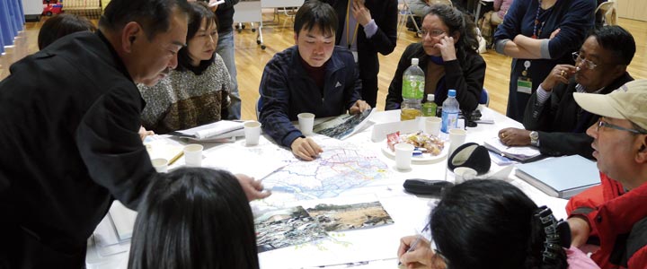 研修員に被災直後の写真や復興計画の地図を見せつつ、これまでの歩みを語る東松島市の住民たち
