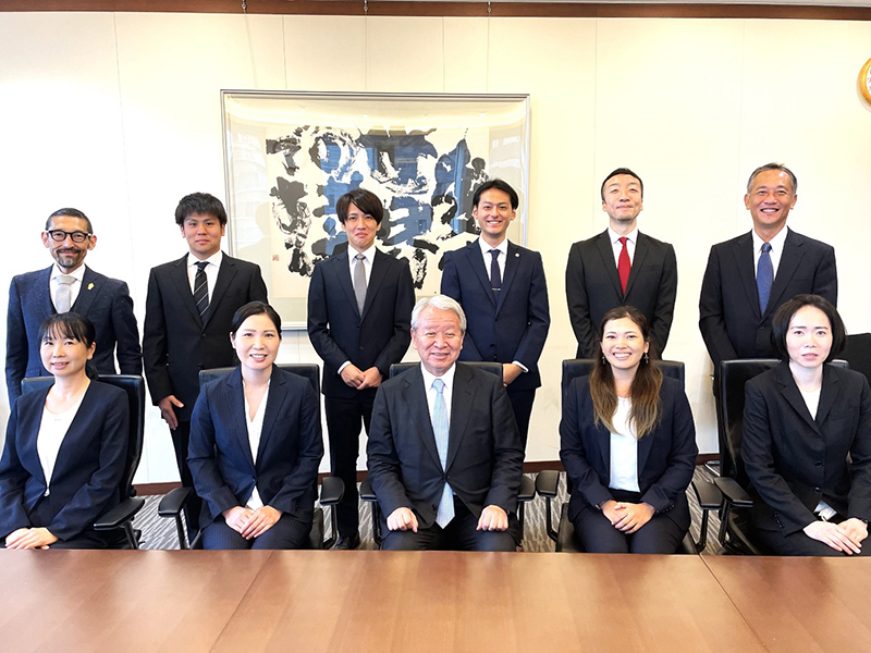 From left in the front row are Ms. Matsuyama; Ms. Fukasawa; JICA President Tanaka; Ms. Murakami; and Ms. Onizuka. In the back row from left are Mr. Otsuka, Chief Secretary of the Office of the President; Mr. Yamazaki; Mr. Sonoo; Mr. Ozaki; Mr. Chiba; and Mr. Tachibana, Director General of JOCV.