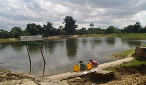 植林用機材として供与してブルドーザーで掘られたため池の水を汲む村の子供たち