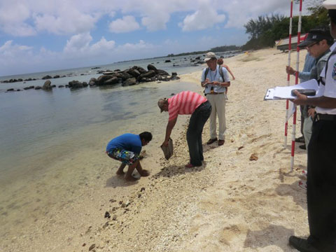 環境省の担当者に、海浜砂の性質や大きさを調べるための調査方法を教えながら、砂を採取している様子。