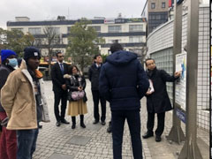 平井駅前の広場に設置された水位標（写真右端）で、海抜ゼロメートル地帯の広がる江戸川区の特徴と、地域の抱える災害リスクについて説明するリバーフロント研究所の土屋氏（右）。足元に濃い青でAP±0mと書かれたところが海面の高さです。