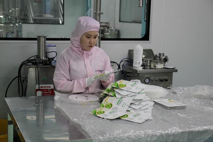 製造されたばかりのフェイスシートを確認しながらパッケージに入れていく女性