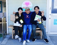 伊予市では住民に親近感を持ってもらうため、実習生にニックネームをつけている。木下るさかさん（キルギス派遣予定／青少年活動、写真左）は名前から「るーちゃん」、沖縄出身の中山 慎さん（タイ派遣予定／野球、写真右）は「シーサー」だ。中央は受け入れ先の一般社団法人いよのミライカイギの冨田 敏代表理事
